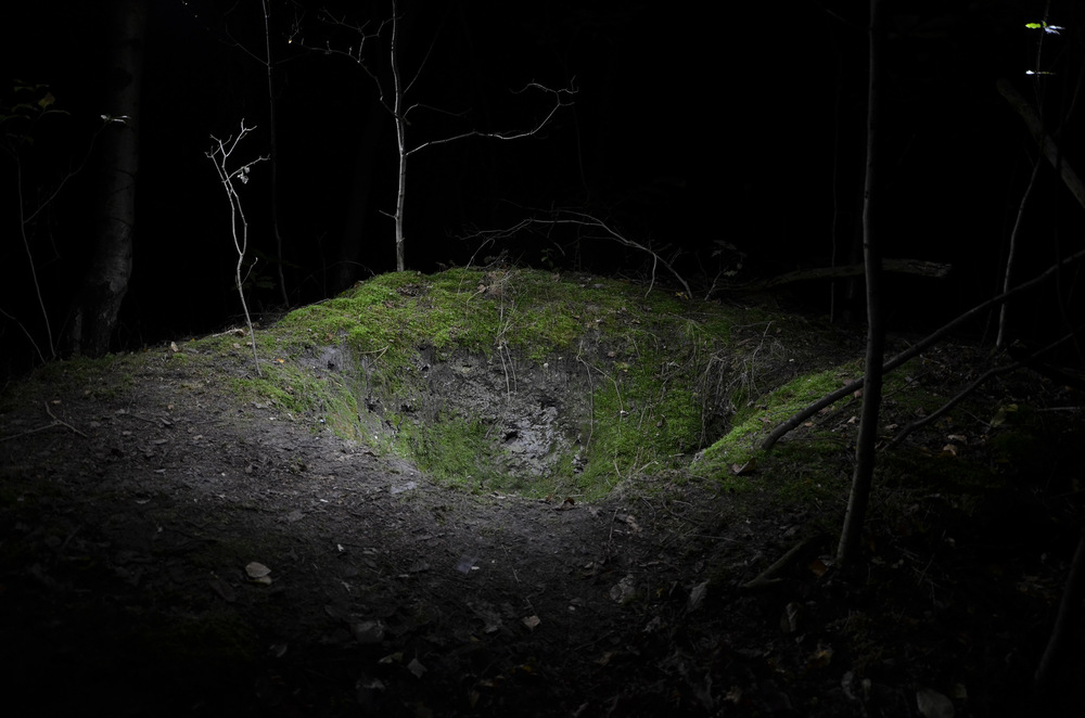 Dennis Ramaekers - Residue Chromiak & Ramaekers 2014 Whilst walking in the forest surrounding my neighborhood, we would often come across small mounds of a very fine, grey powder. We soon found out this powder was a residue, called flyash. We discovered if you would dig random holes, most of the time you would find this substance. Residue is a photograph taken of a pit we found in this forest. We detonated some small explosives in the pit and recorded the blast. Afterwards, when the dust had settled, we started taking pictures. One of these pictures was printed and placed into a lightbox which is shown in combination with a modified version of the sound of the explosion and the background noises before and after the explosion.