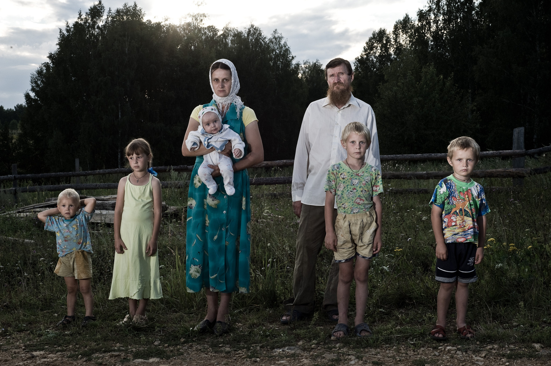 Konstantin Salomatin - Bronnikov family (from left to right) - Filipp, Mariamna, Daria with a newborn Feoklist, Aleksey, Vladimir and Gleb..Daria: People come to die here. It is already the end of the world as it is for them. They feel very dark. But you know, after a year they start to change, Even their posture changes. They start to smile, reconstruct the house, get cattle, have new kids.. Have a life, after the end. They are still ready for it, but they hope it wont come that soon. ..Some say its better to get rid of the passports, but I cant really do it. We might need to purchase a car, new house..while waiting.. Alexey didnt have passport before (because there is a daemons number in the code - 666), but now he has changed his mind. Kremenki settlement, Nizhny Novgorod region. Diveevo. Russia 2012