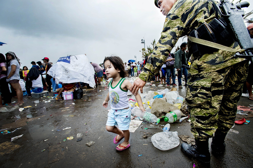 John T. Pedersen Photography - 2013 She survived People gather at Tacloban airport waiting for evacuation. A little girl is taken care of by a soldier.